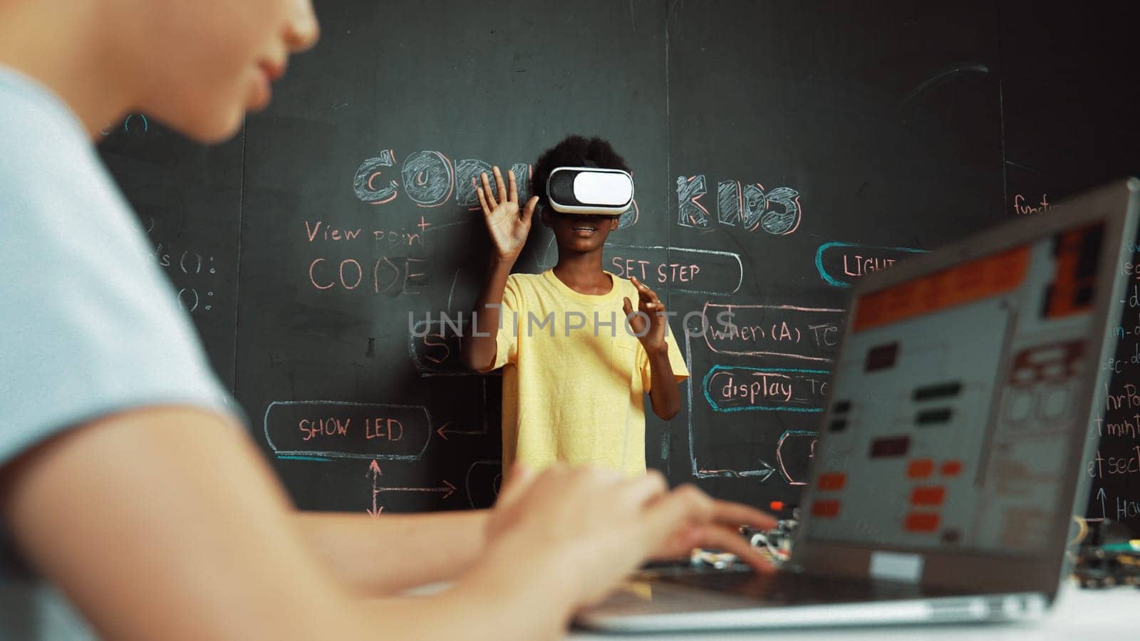 Closeup of school girl hand coding program while african student using VR interact with metaworld. Smart boy wearing virtual reality glasses and playing video games at innovative class. Edification.