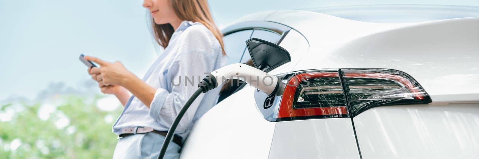 Young woman using smartphone to pay for electric car charging. Exalt by biancoblue