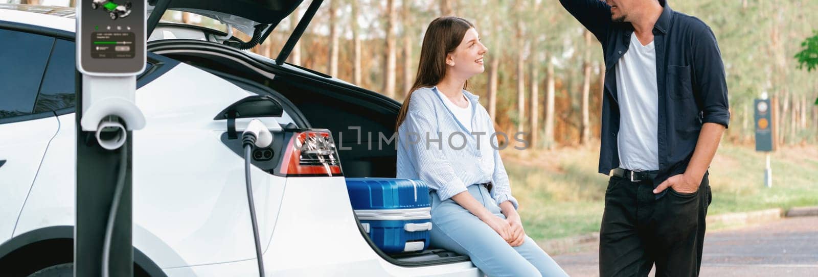 Lovely young couple recharging battery for electric car in autumn. Exalt by biancoblue