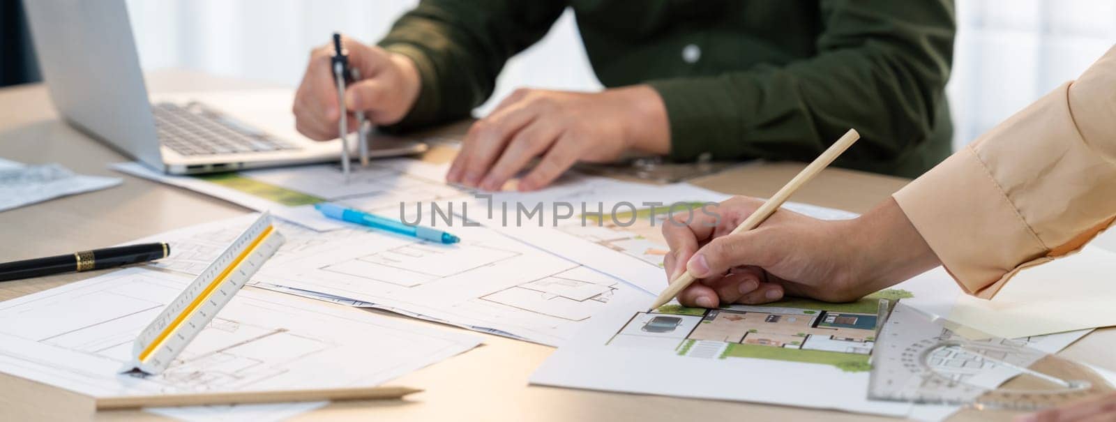 A cropped image of professional engineer using divider to measure blueprint at meeting table with blueprint, laptop and architectural equipment scatter around. Closeup. Delineation.