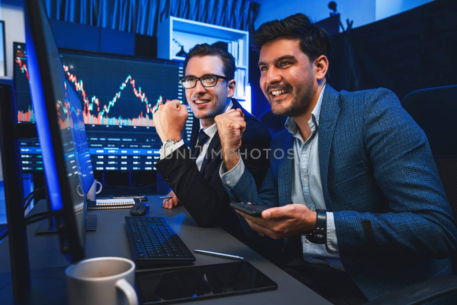 Two stock exchange traders comparing dynamic investment graph via phone and pc with high profit in currency rate. Showing financial benefit data on monitor screen in neon light at workplace. Sellable.