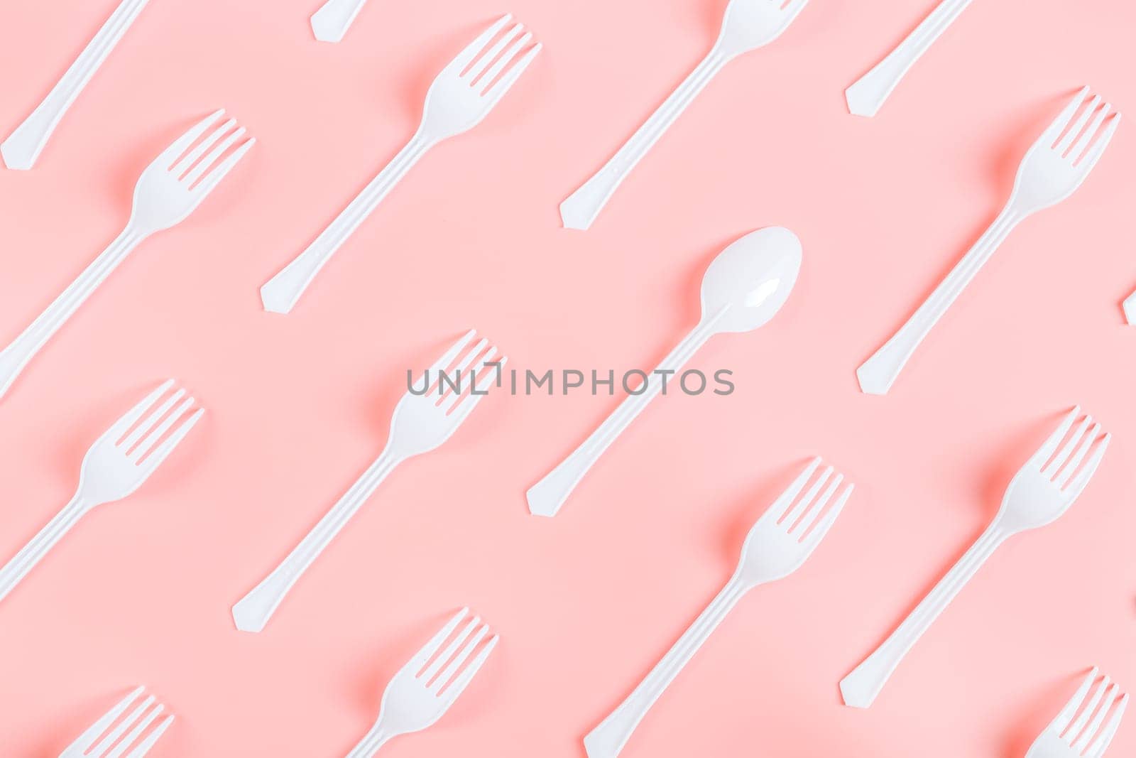 White plastic forks with one spoon lie diagonally on a pink background, flat lay close-up. Ecology concept, template, banner.
