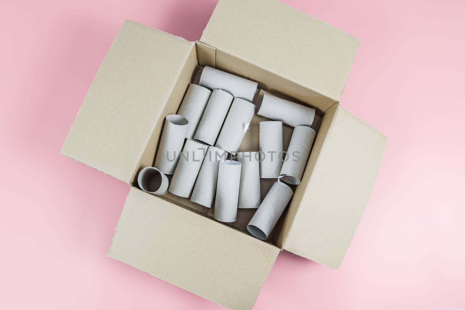 Empty toilet paper rolls lie in a cardboard box on a pastel pink background close-up, flat lay closeup. The concept is environmentally friendly, waste sorting and recycling.