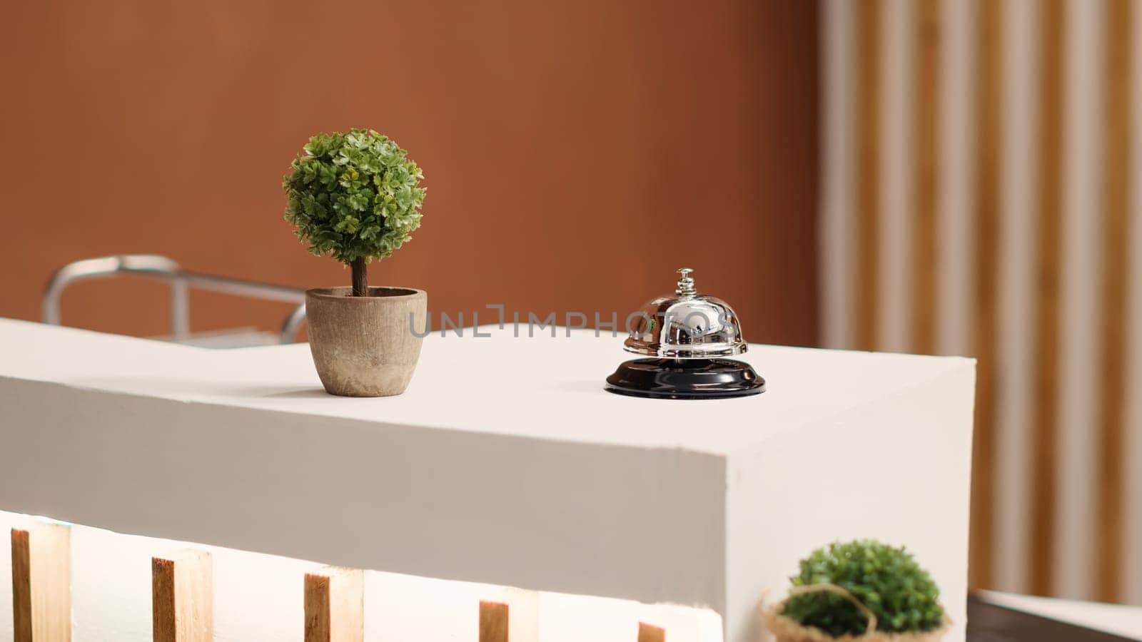 Elegant concierge bell on modern stylish hotel lobby check in desk. Reception bell next to mini plant on empty warm hospitality industry lounge reception counter, close up