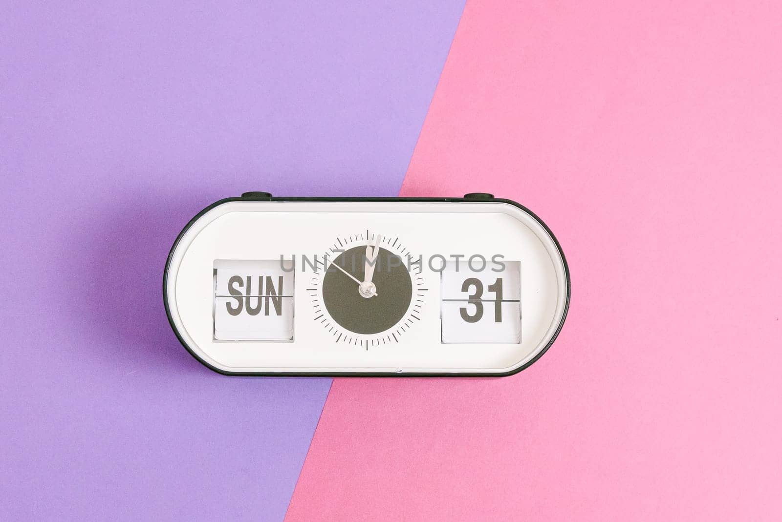 One alarm clock with the date and time of Easter 2024: Sunday March 31 lies in the center on a lilac pink background, flat lay close-up. Concept reminder, holiday time.
