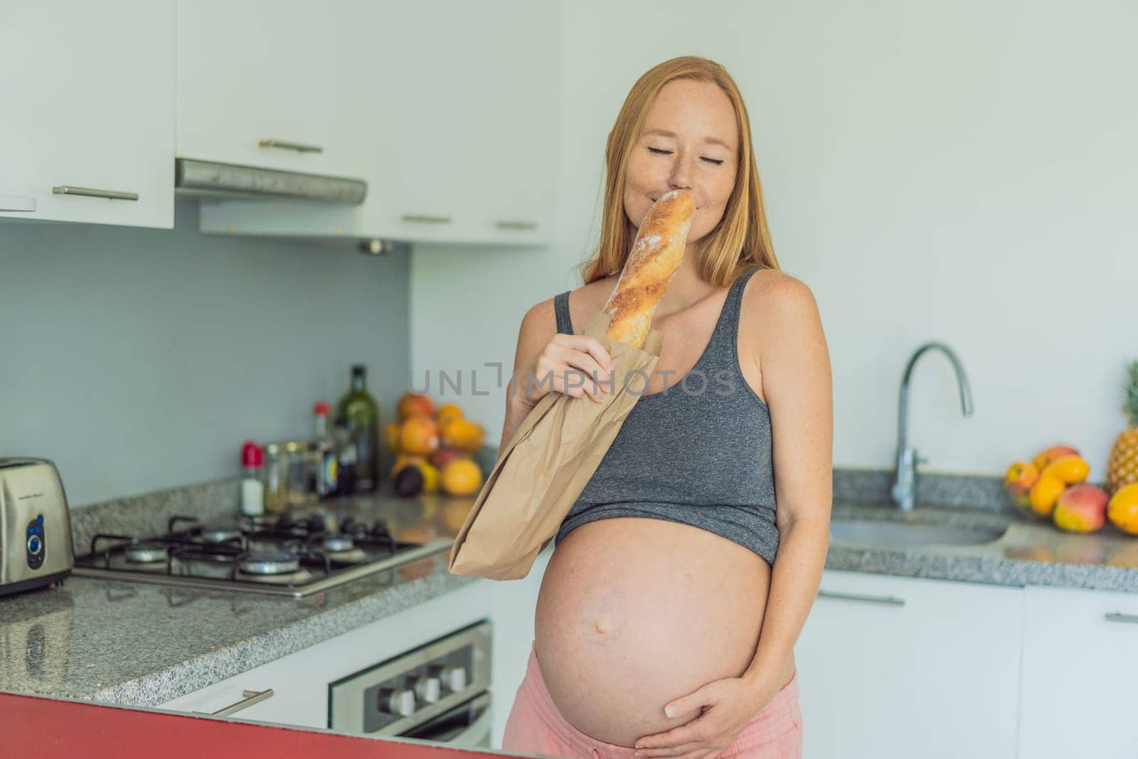 Pregnant woman eating bread in the kitchen. Exploring the impact of gluten during pregnancy: understanding the potential benefits and risks for maternal health and fetal development by galitskaya