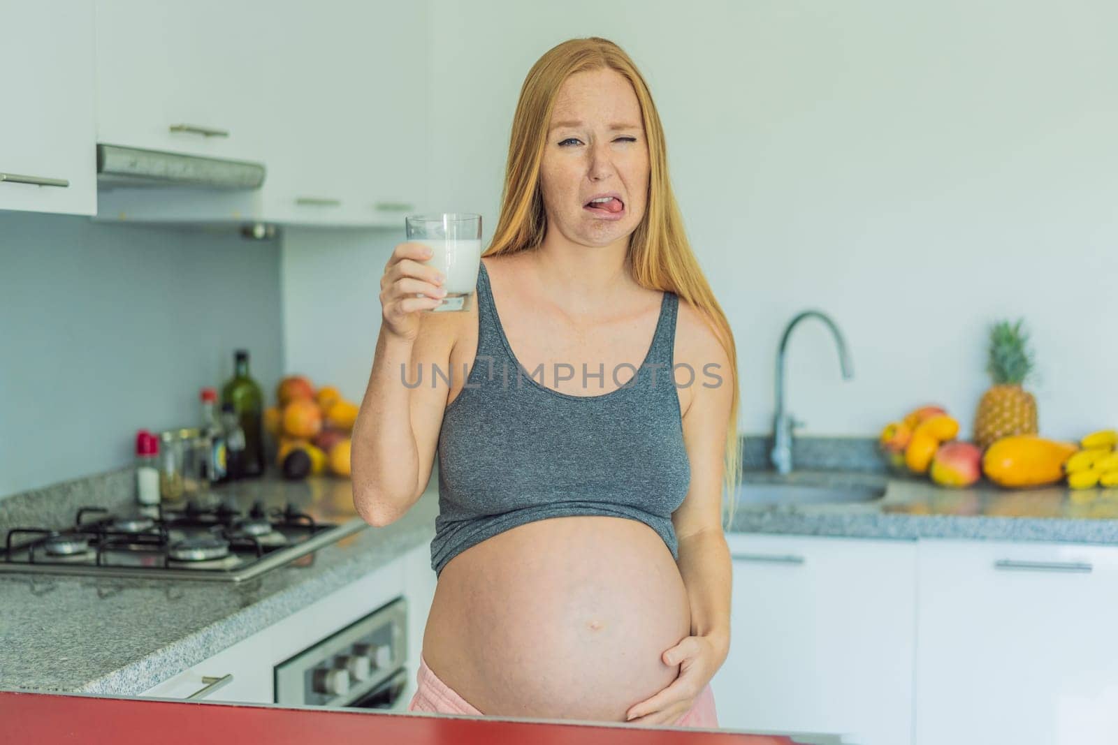 Weighing the pros and cons of milk during pregnancy, a thoughtful pregnant woman stands in the kitchen with a glass, contemplating the decision to include or avoid milk for her and her baby's well-being.