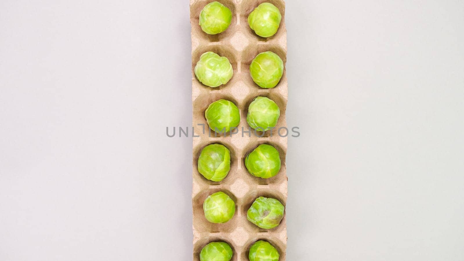 Raw organic Brussel sprouts in brown egg container on grey background, top view. Flat lay, overhead, from above. Copy space