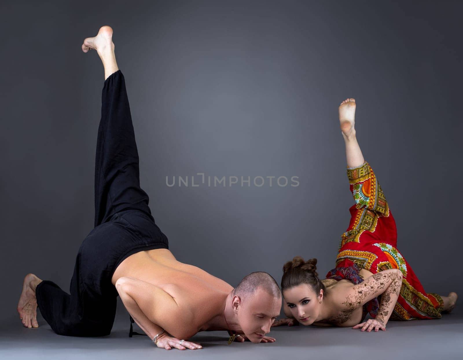 Beautiful couple doing yoga in studio, on grey background