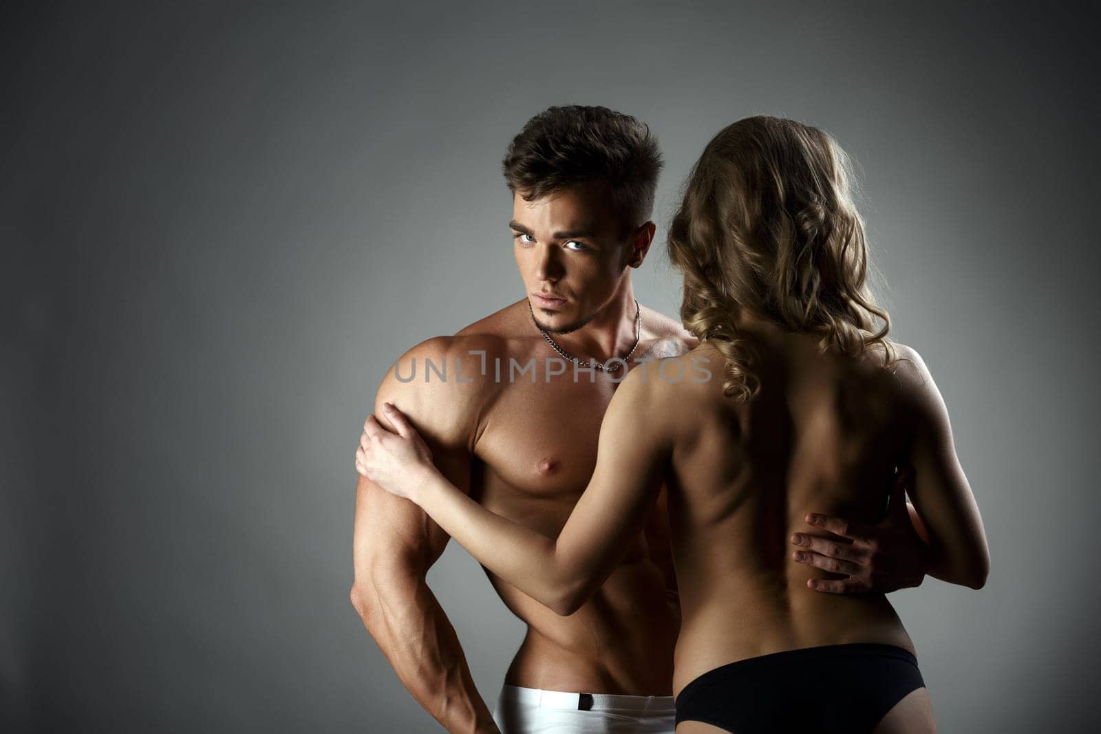 Studio photo of bodybuilder hugs topless model, on gray background