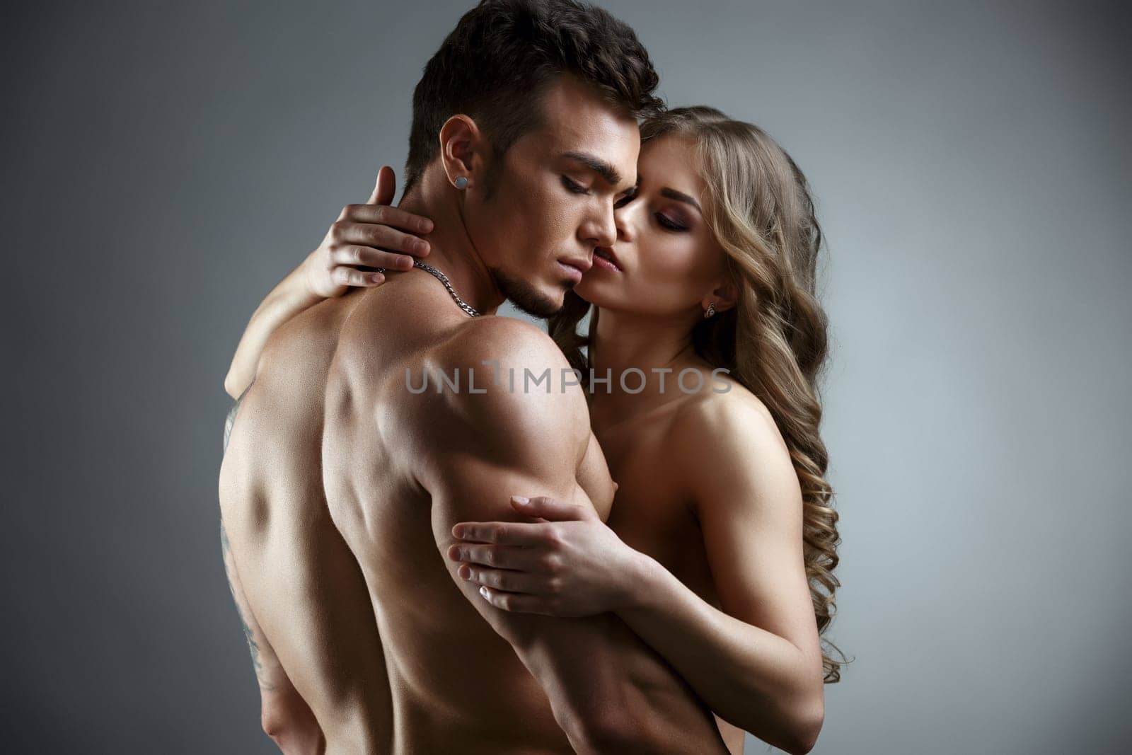Erotica. Embrace of attractive nude couple. Studio photo, on grey backdrop