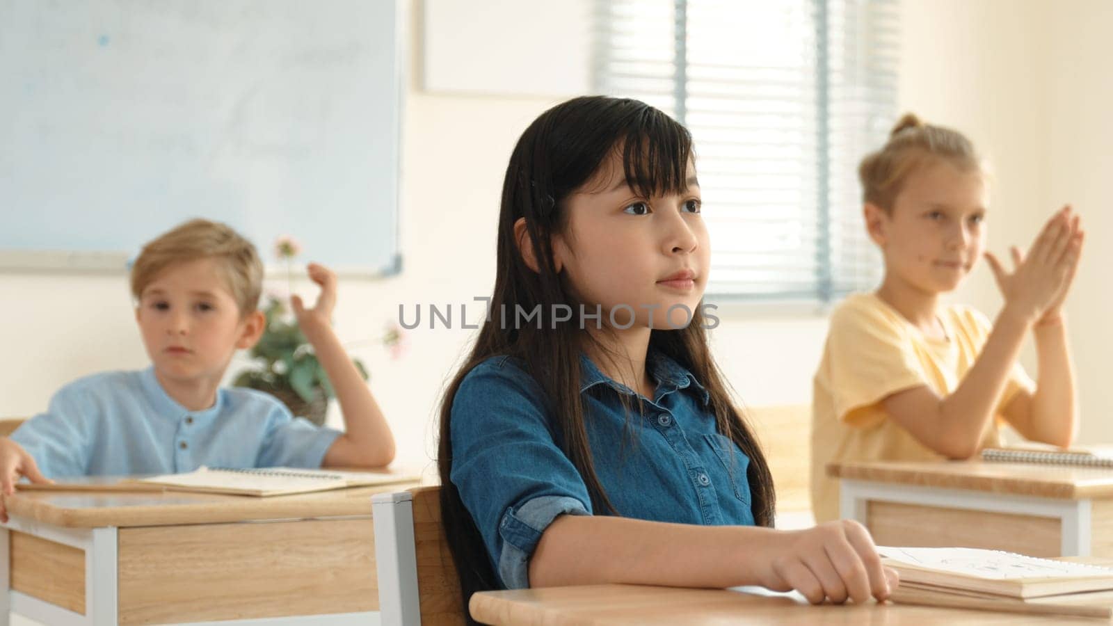 Smart elementary student looking at teacher while attend in classroom. Diverse smart student sitting at classroom while listening teacher explain about classwork or test. Education concept. Pedagogy.