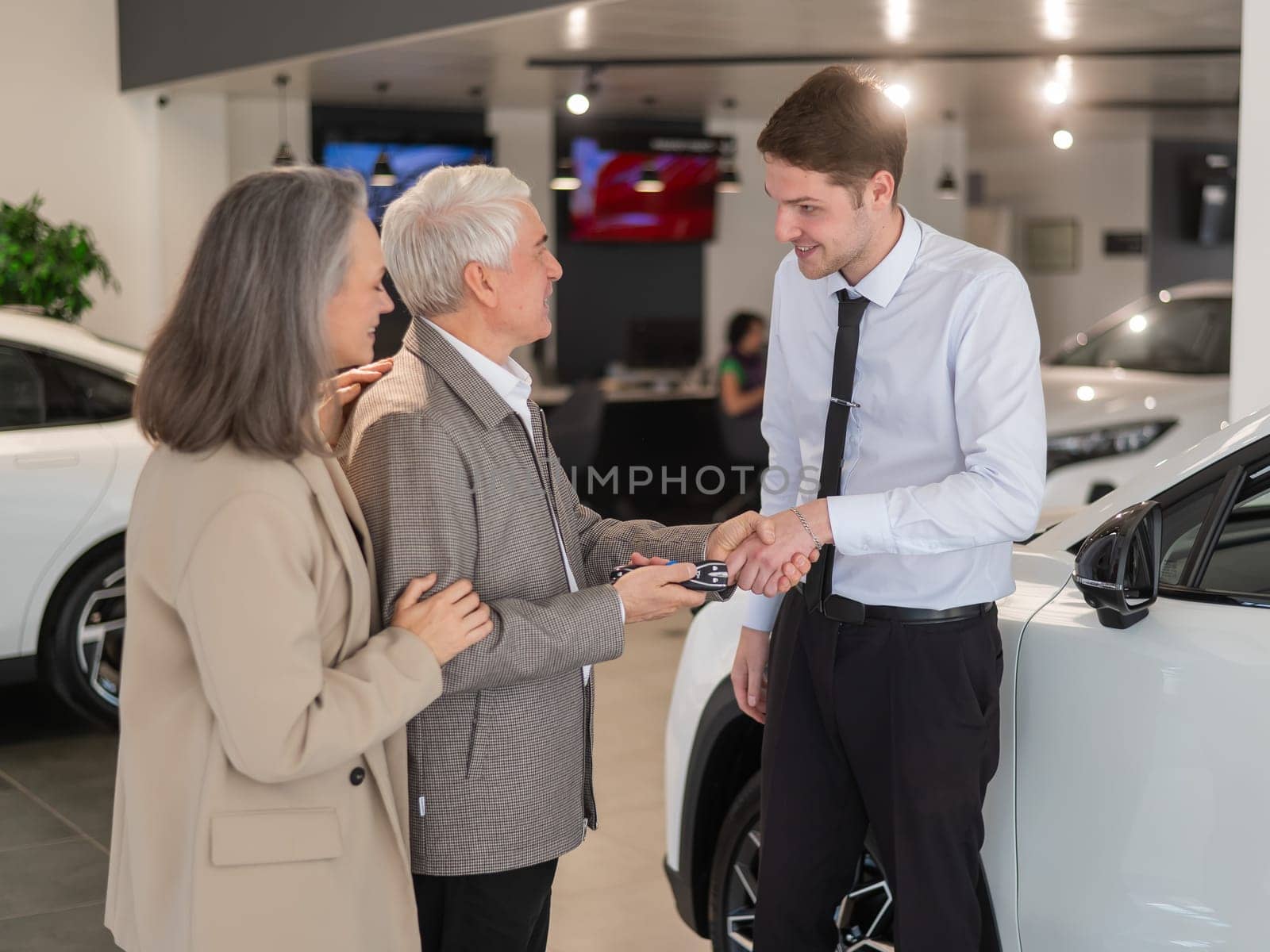 A salesman hands over the keys to a new car to an elderly Caucasian couple