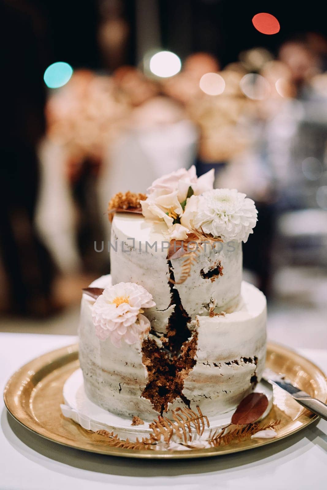 Two-tier wedding cake decorated with flowers with a cut out sector stands on a tray on the table. High quality photo