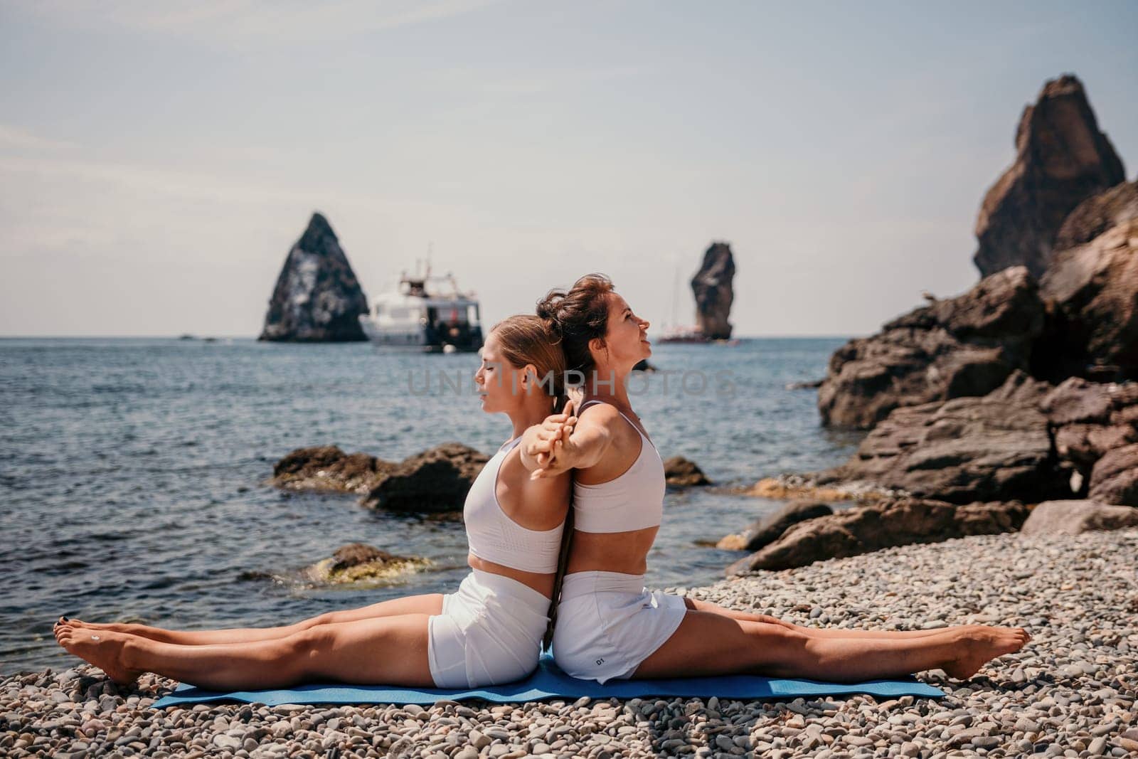 Woman sea yoga. Two Happy women meditating in yoga pose on the beach, ocean and rock mountains. Motivation and inspirational fit and exercising. Healthy lifestyle outdoors in nature, fitness concept. by panophotograph