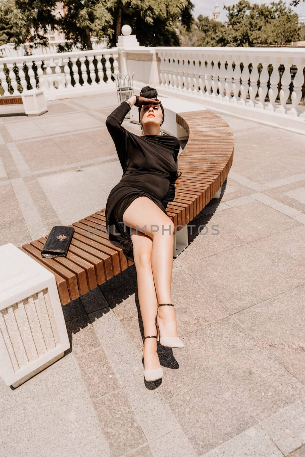 Stylish woman in the city. Fashion photo of a beautiful model in an elegant black dress posing against the backdrop of a building on a city street by Matiunina