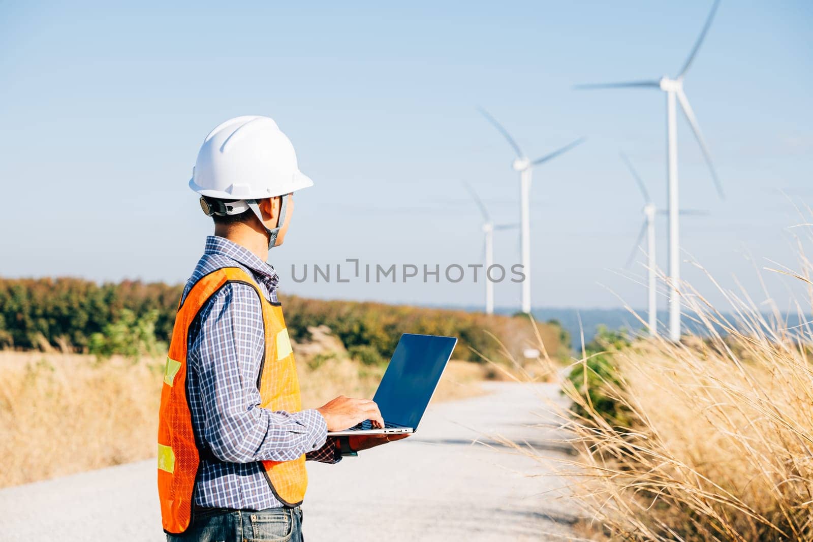 Engineer with laptop by wind turbines by Sorapop