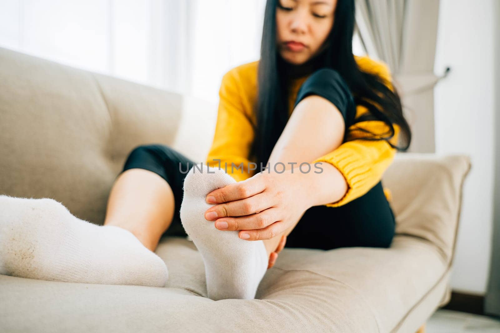 A woman on a sofa massages her painful foot emphasizing the highlighted pain area by Sorapop