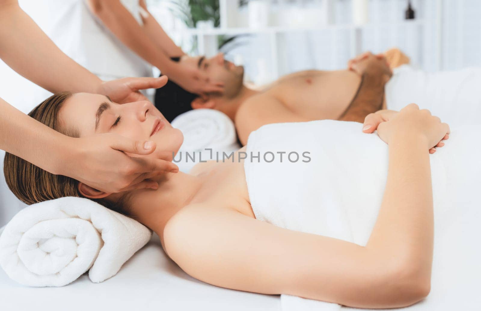 Caucasian couple enjoying relaxing anti-stress head massage and pampering facial beauty skin recreation leisure in dayspa modern light ambient at luxury resort or hotel spa salon. Quiescent