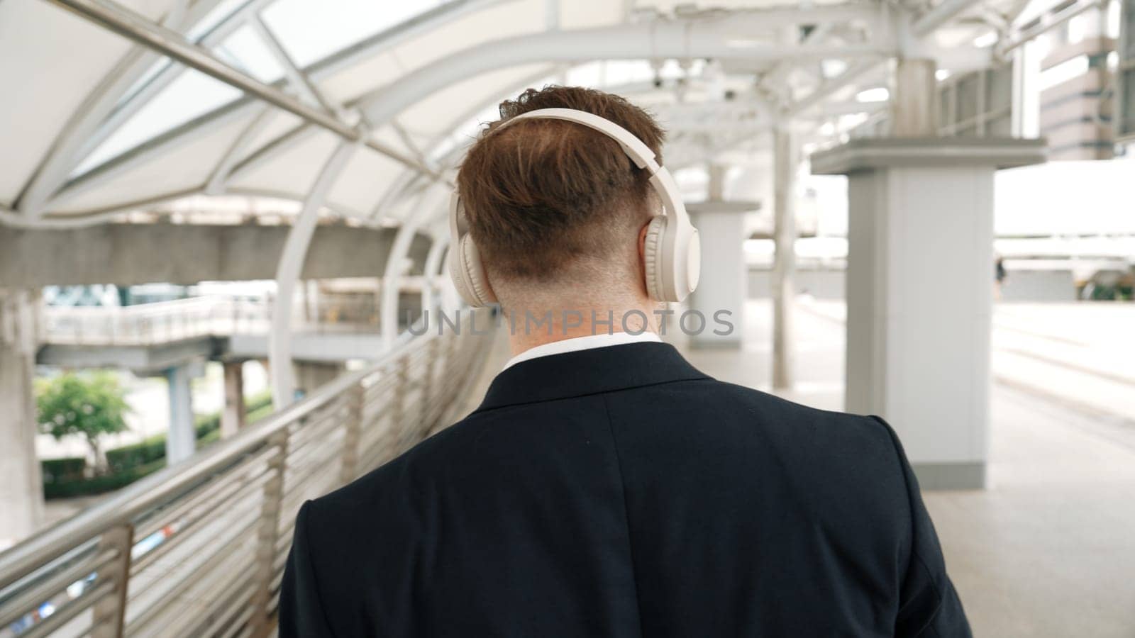 Happy business man dancing while wear headphone at bridge in urban city. Energetic manager motivation performance moving to music to celebrate successful project while walk along. Back view. Urbane.