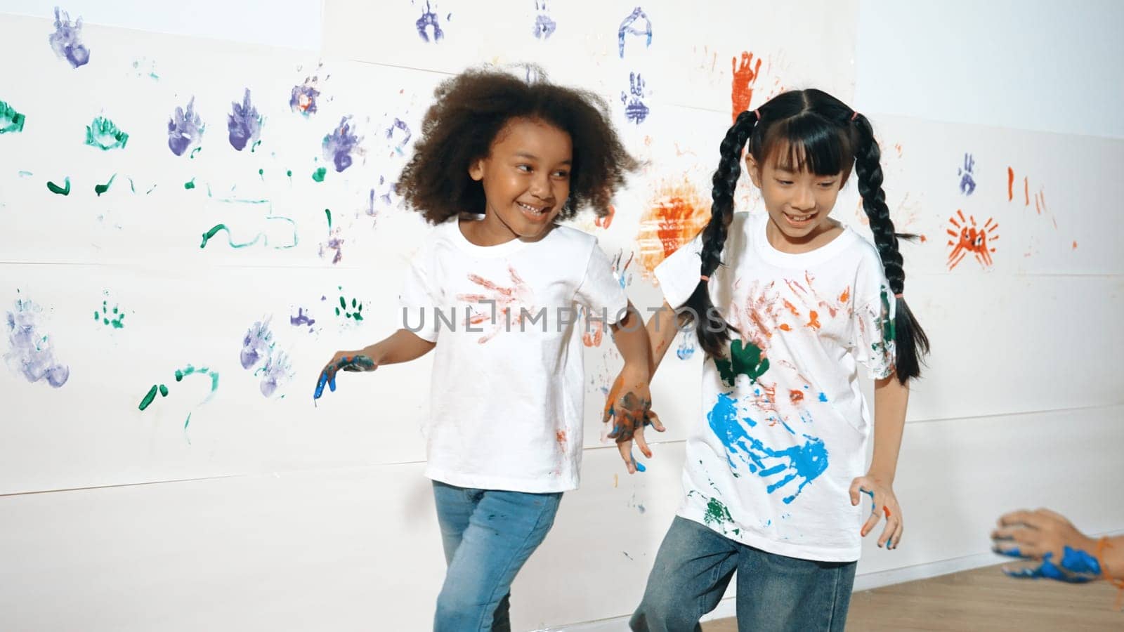 Playful children playing and running with colorful stained hand in front of white background. Funny happy multicultural students enjoy attending in art lesson. Creative activity concept. Erudition.