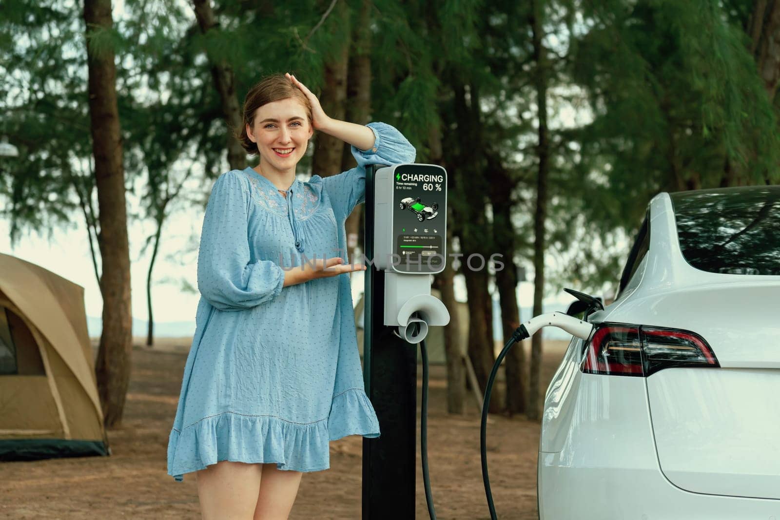 Holiday road trip vacation traveling to the beach camp with electric car, young woman recharge EV vehicle with green and clean energy. Beach travel camping with eco-friendly EV car .Perpetual