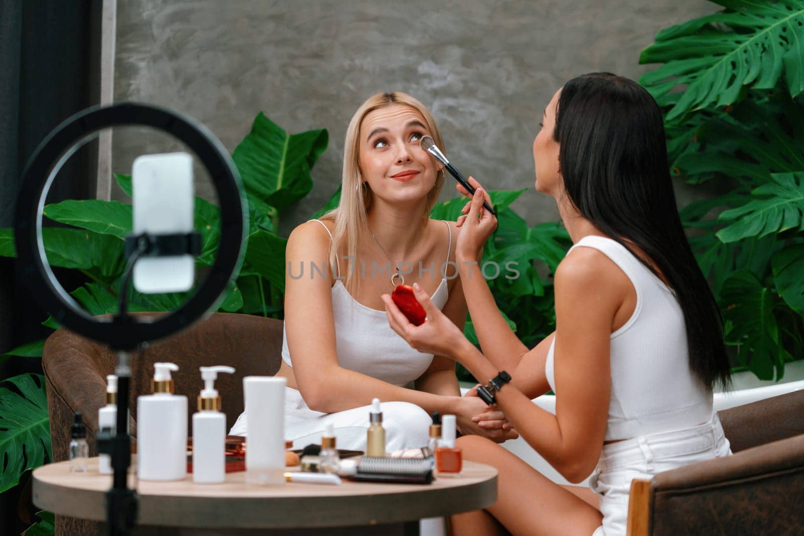 Two beautiful content creator making natural beauty and cosmetic tutorial on green plant garden video. Beauty blogger use camera light ring to show how to beauty care to social medial audience. Blithe