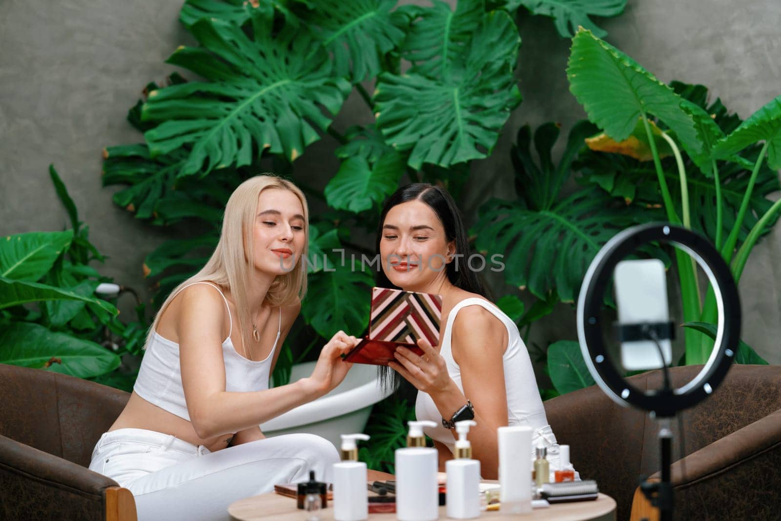 Two beautiful content creator making natural beauty and cosmetic tutorial on green plant garden video. Beauty blogger showing how to beauty care to social medial audience using selfie stick . Blithe