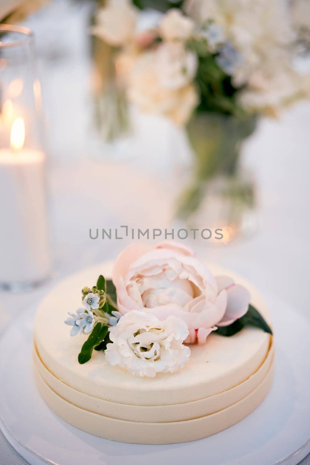 Wedding cake decorated with flowers stands on a stand on the table by Nadtochiy