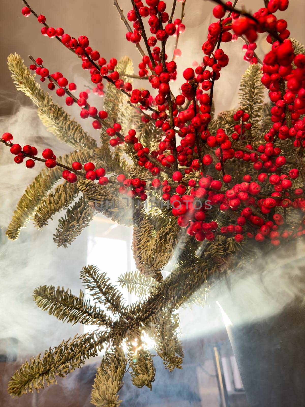 a bouquet of branches with red berries and fir branches in smoke in sunny weather, the rays of the sun through the branches. High quality photo