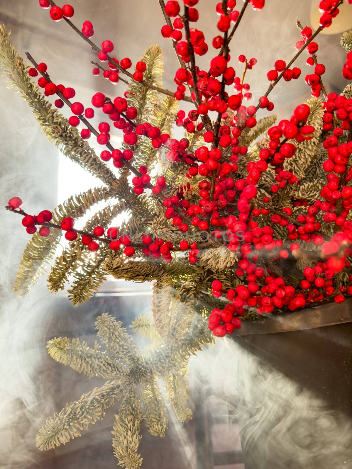 a bouquet of branches with red berries and fir branches in smoke in sunny weather, the rays of the sun through the branches. High quality photo