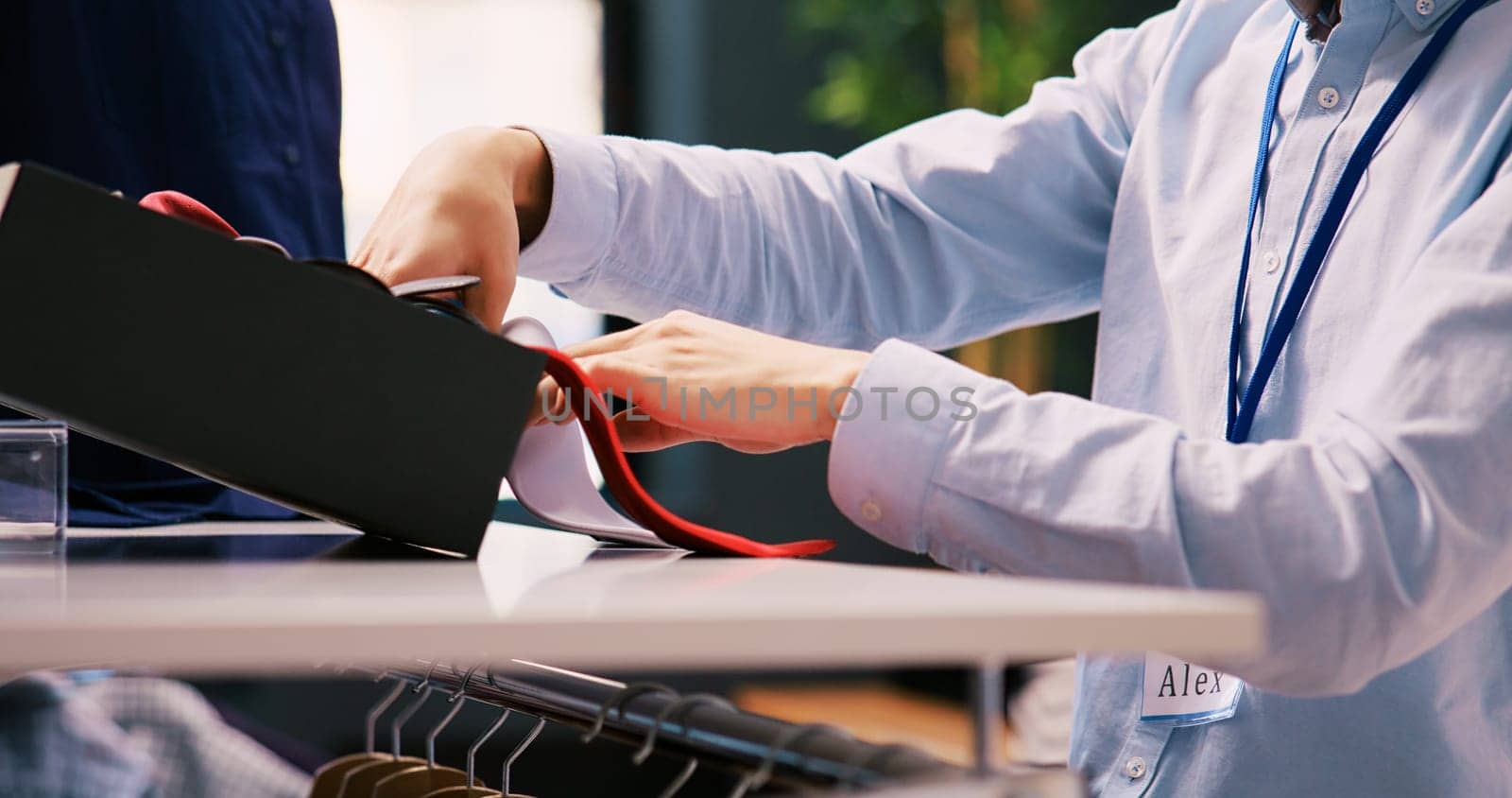 Asian worker wrapping elegant tie, working at modern boutique visual. Stylish manager arranging hangers and racks full with fashionable merchandise in shopping centre. Fashion concept