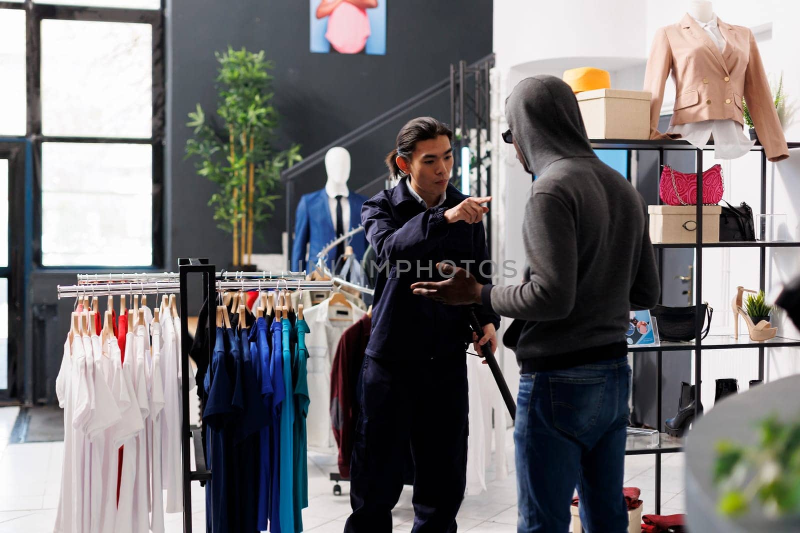 Thief was caugh robbing store by worker, asking him to return stylish clothes or will call the police in clothing store. African american robber trying to steal fashionable merchandise