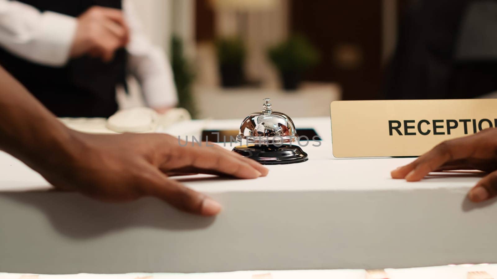 Close up of african american guests ringing concierge bell at reception counter during check in process. Vacation trip tourists ready to book in their reservation at hotel lounge front desk