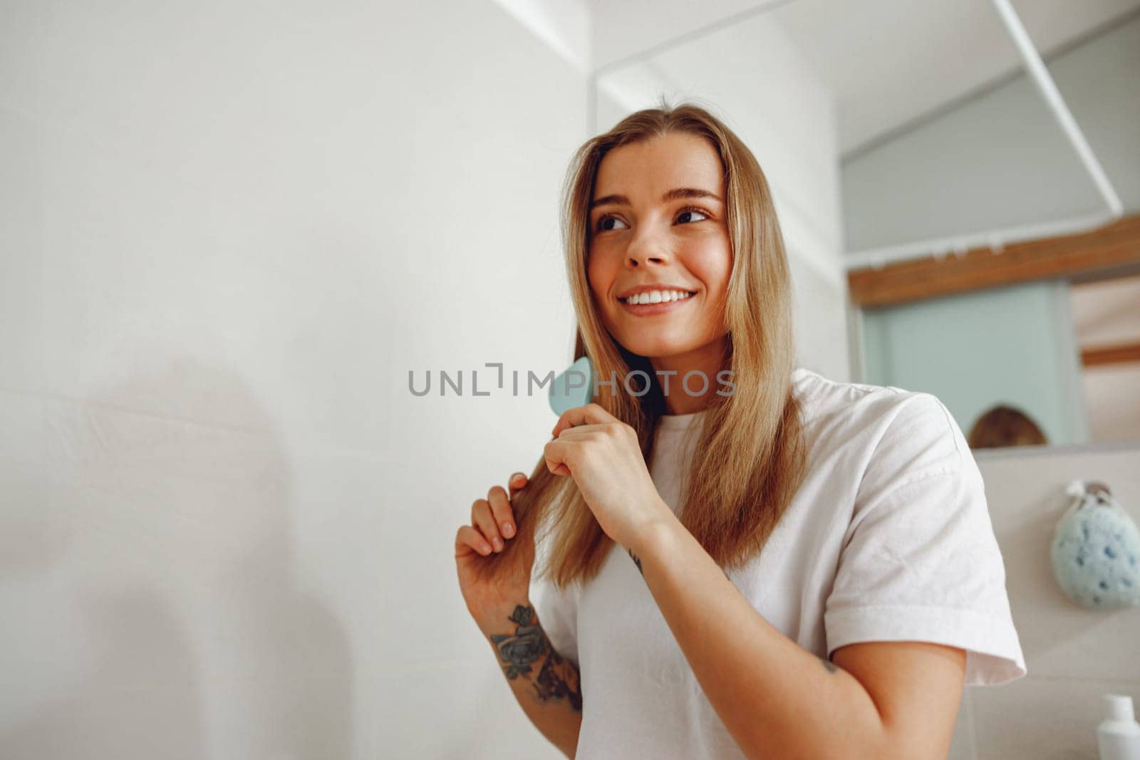 Woman standing in front of mirror at bathroom and combing her hair with brush after shower by Yaroslav_astakhov