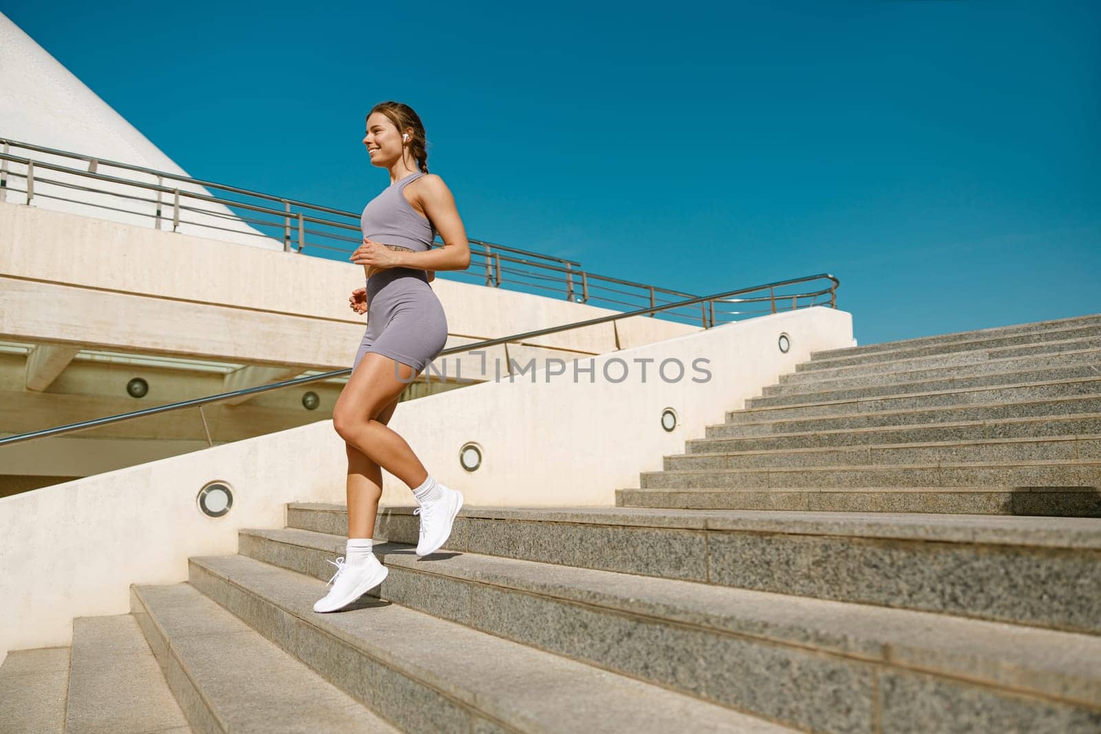 Active female athlete in sportswear running on steps outdoors on a sunny day. Reaching the goal by Yaroslav_astakhov