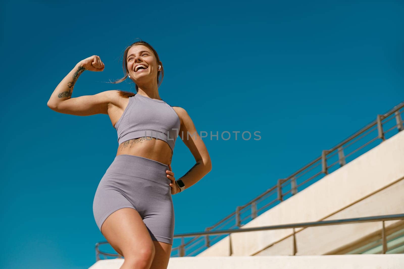 Female model in sportswear showing biceps standing outdoors and looks away by Yaroslav_astakhov