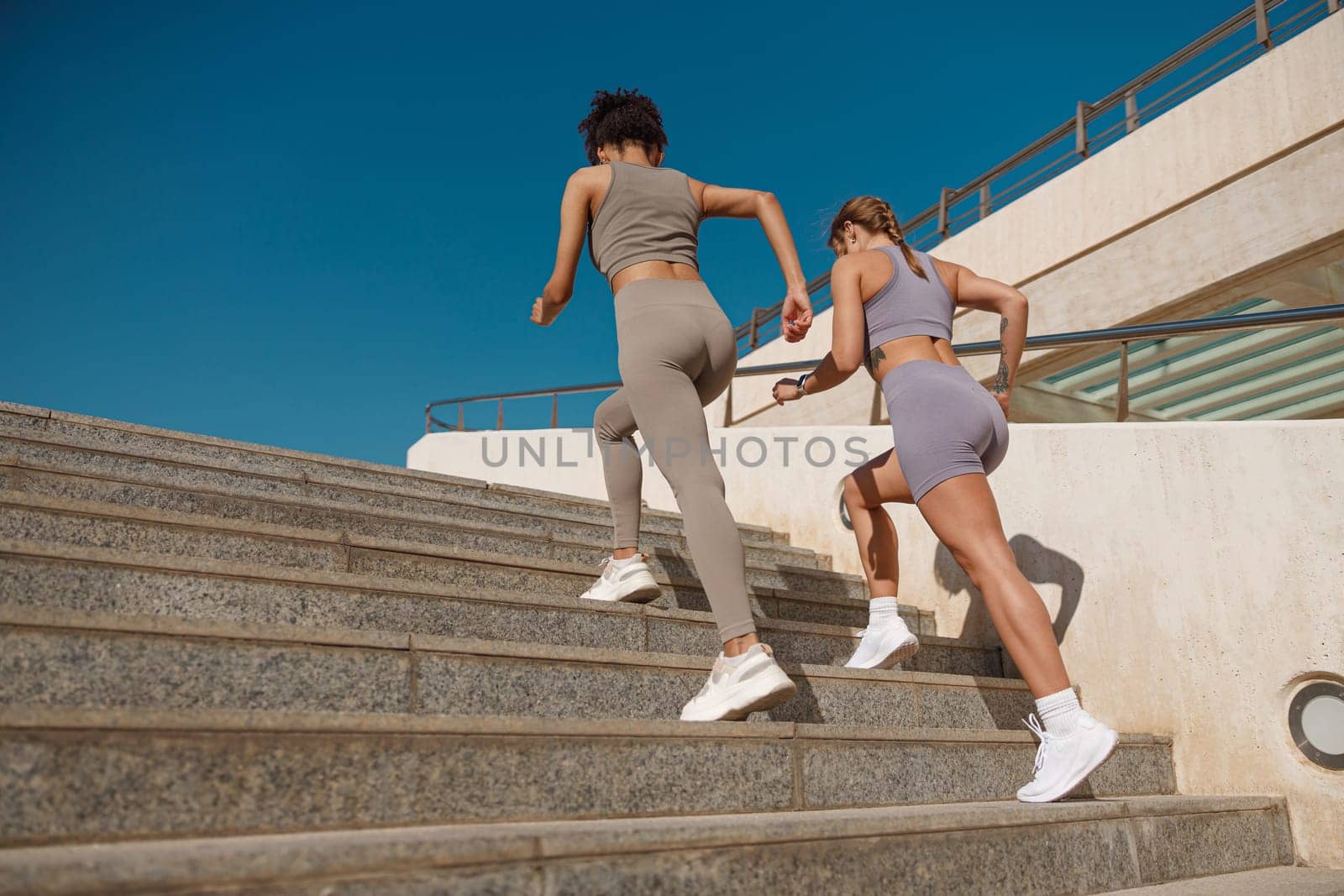 Two active female athlete friends in sportswear running on steps outdoors on a sunny day