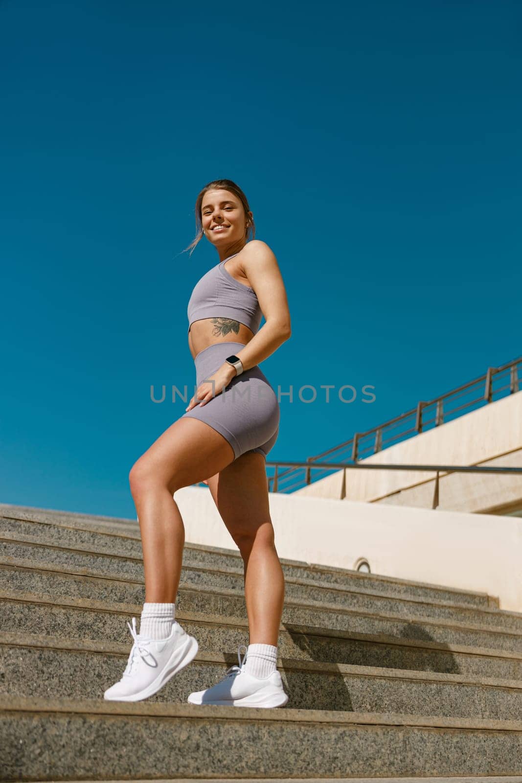 Smiling woman in sportswear have a rest after workout outside standing on stairs background
