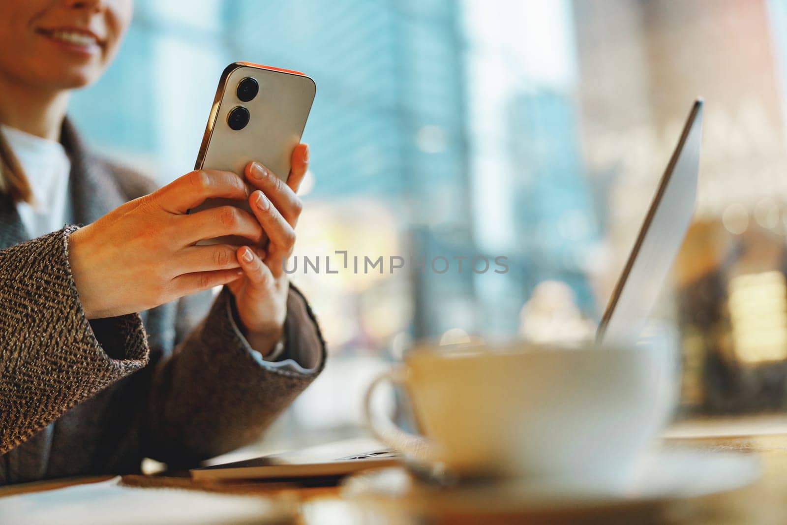 Woman manager reading message on phone and work on laptop in cafe. Distance work concept