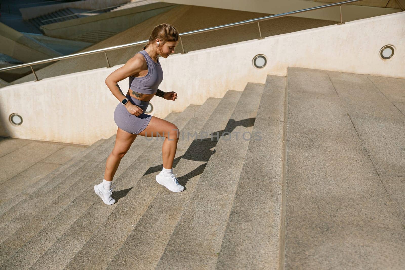 Side view of female athlete in sportswear running on steps outdoors on sunny day. Reaching the goal by Yaroslav_astakhov