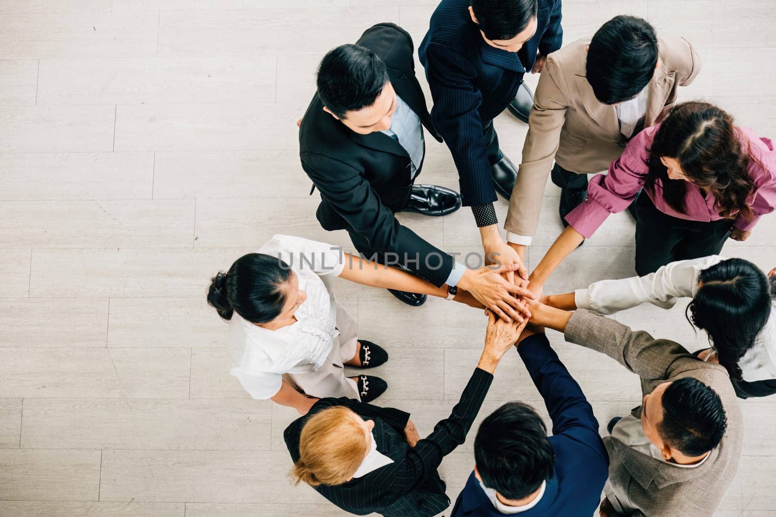 A top view shows four diverse businesspeople forming a circle stacking their hands. This embodies the concepts of unity teamwork and global collaboration in the corporate world.