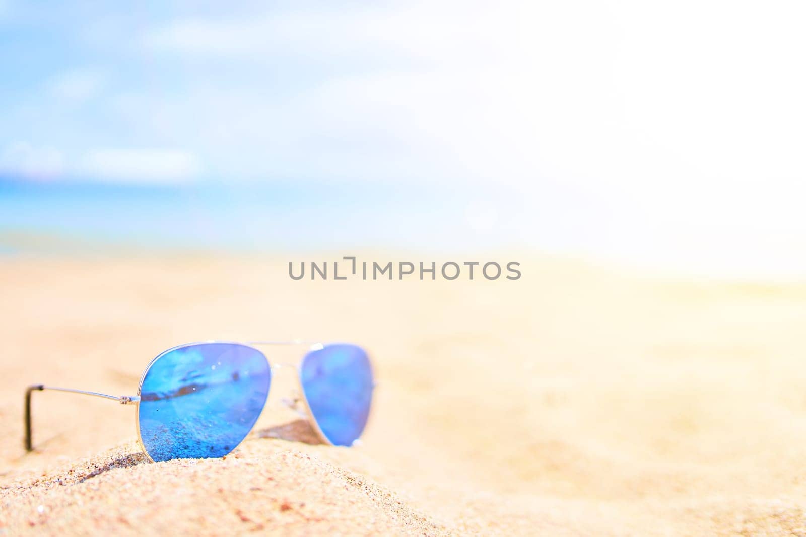 Sunglasses on the sand with ocean and sky on background