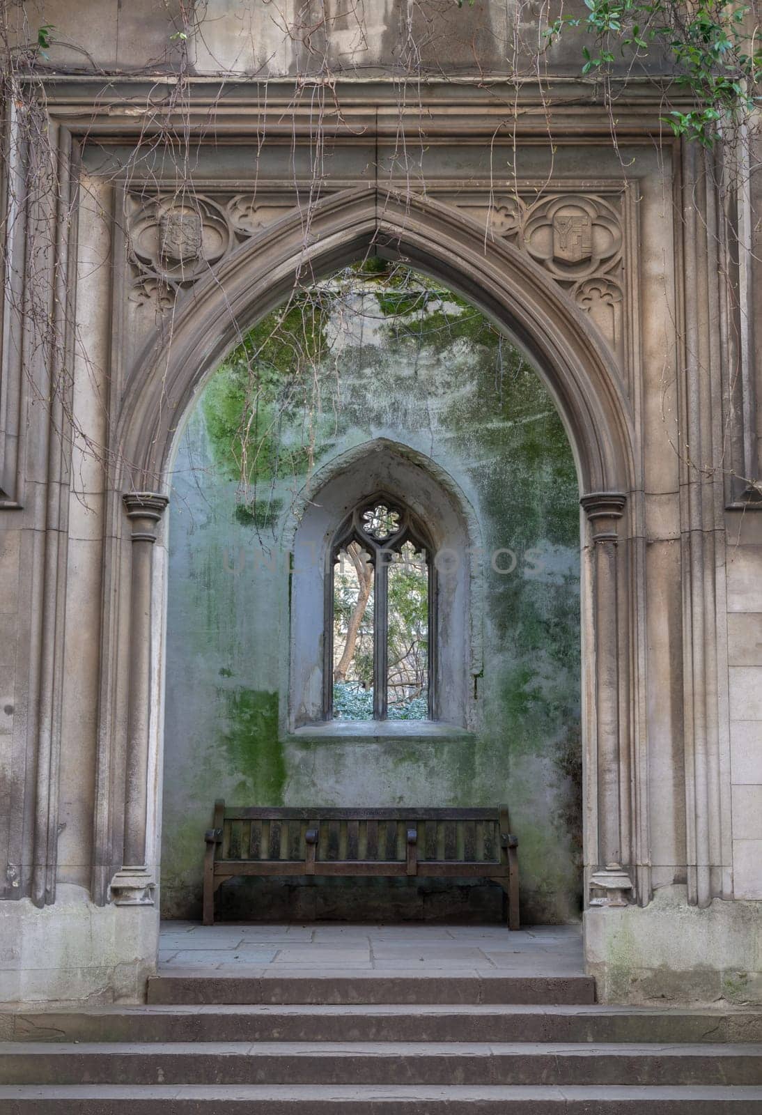 London, UK - Feb 27, 2024 - Stone staircase leads to The stone arched entrance inside of St Dunstan in the East Church Garden with Stone window frame and Wooden benches. The historic church was bombed and destroyed in the Second World War and is now a park, London city hidden places, Space for text, Selective focus.