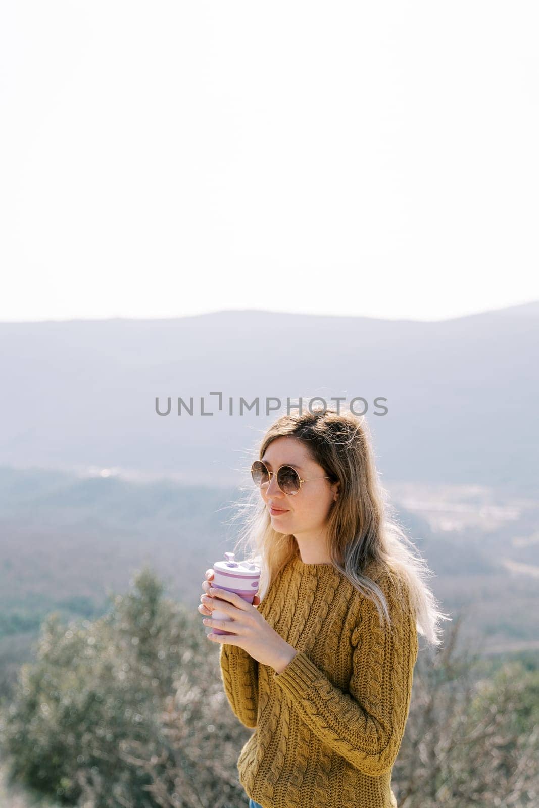 Smiling female traveler with a glass of coffee stands on a mountain. High quality photo