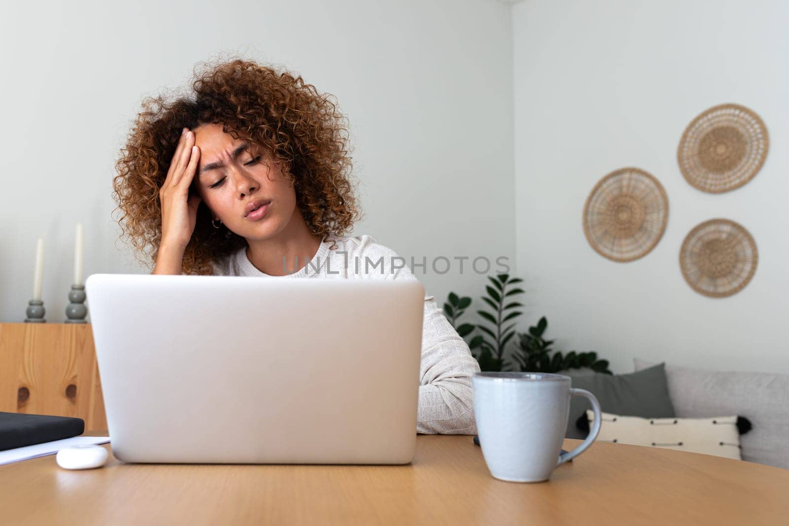 Multiracial woman feeling tired and having headache at home office. Overwhelmed Hispanic female working with laptop. by Hoverstock
