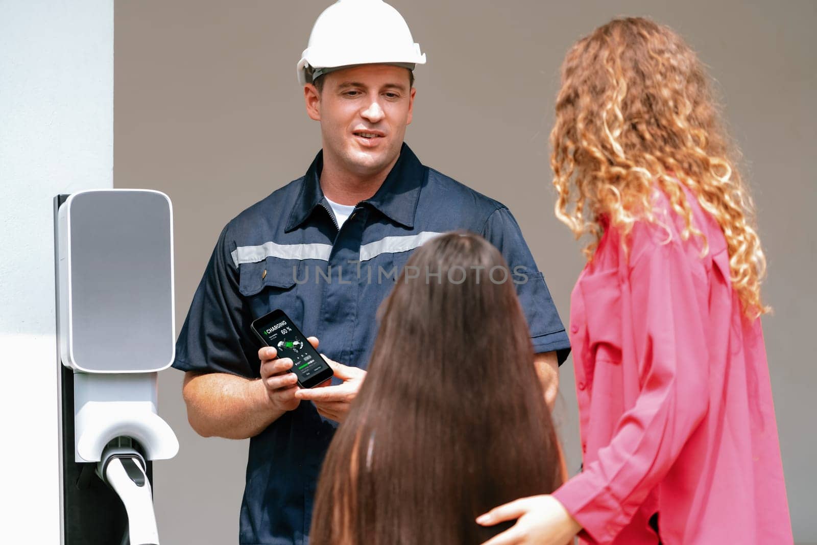 Technician install home EV charging station, providing service support for EV app on customer smartphone for monitoring charging status and set charging schedules at home. Synchronos