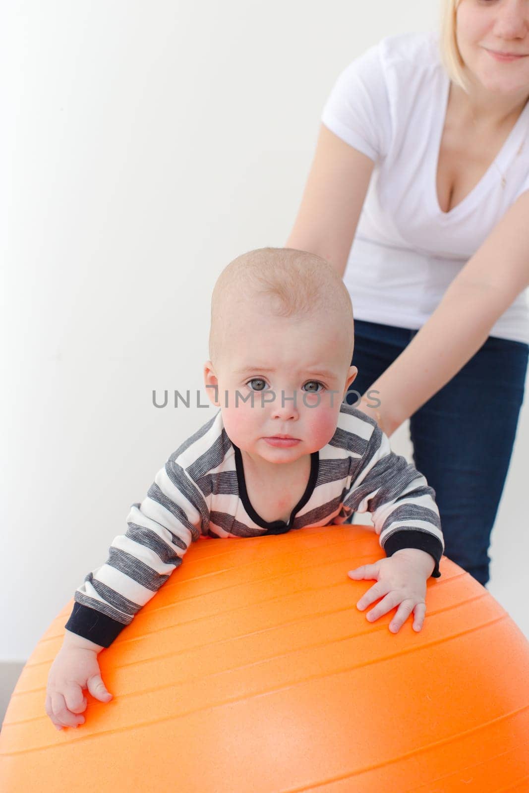 Sad little boy lying on a fitball with the mother support. Vertical studio shot.