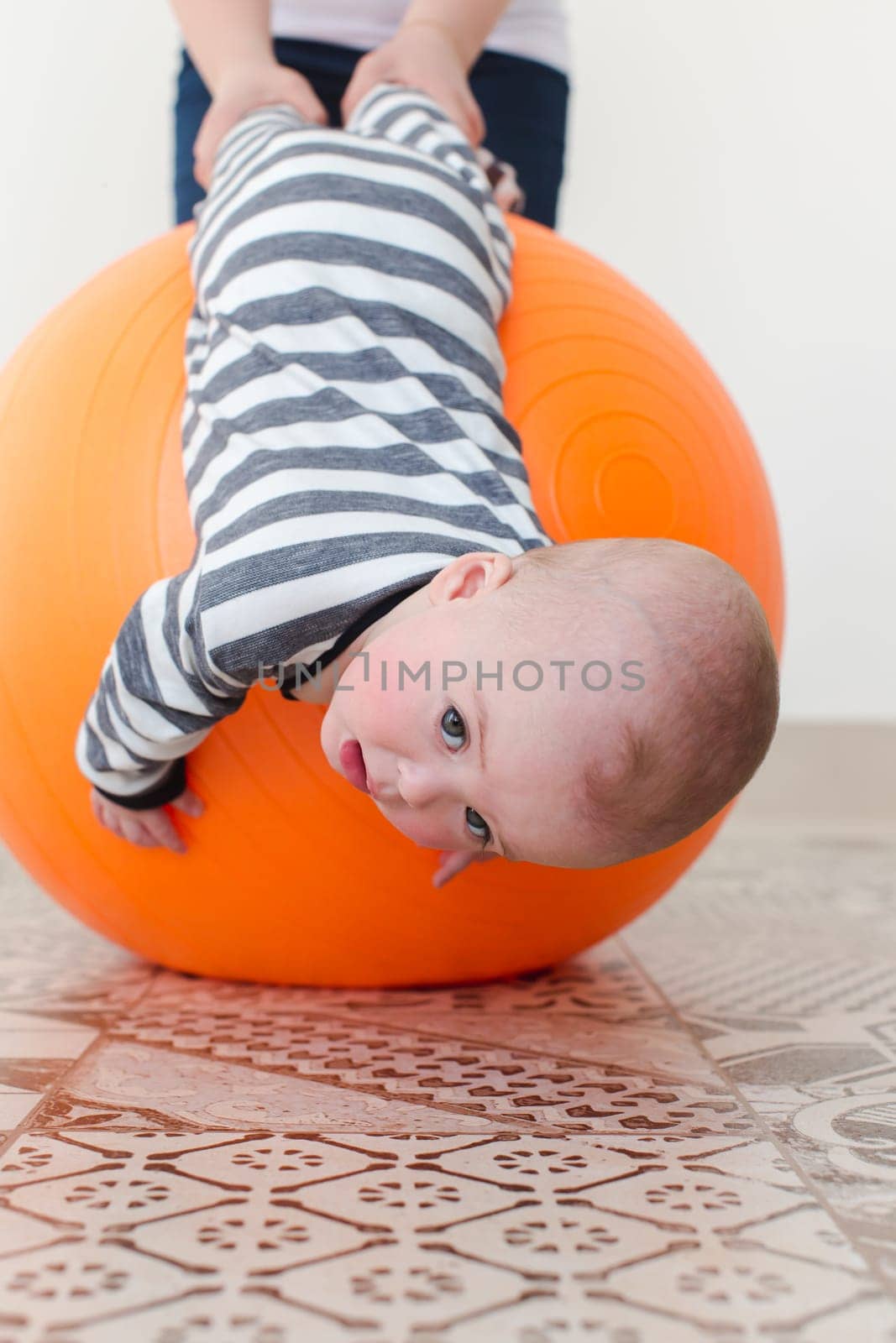 Sad little boy lying upside down on a fitball being supported with a parent.