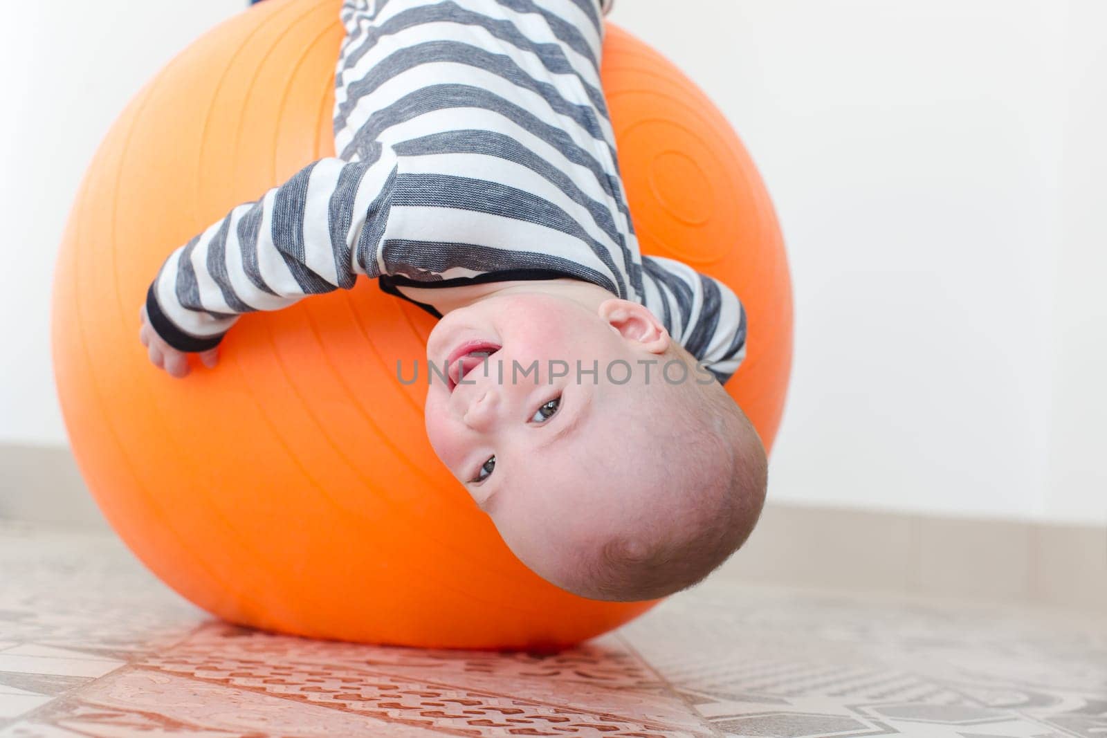 Smiling little boy lying on a fitball upside down. Horizontal studio shot.